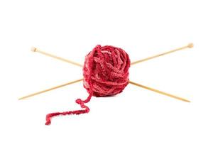 des aiguilles à tricoter percent une pelote de laine rouge.