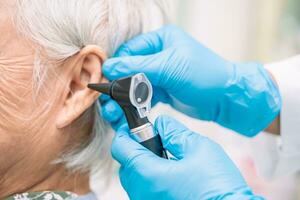 audiologiste ou ent médecin utilisation otoscope vérification oreille de asiatique Sénior femme patient traiter audition perte problème. photo