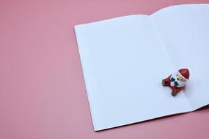 un jouet du père noël assis sur un livre de journal blanc sur fond rose photo