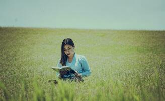 une fille en train de lire une livre dans le champ, une la personne séance sur le herbe en train de lire une livre, attrayant gens séance sur le herbe en train de lire une livre photo
