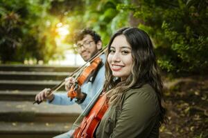 portrait de deux Jeune altistes séance dehors. homme et femme violoniste séance sur le escaliers. deux Jeune violonistes séance en plein air à la recherche à le caméra. concept de deux Jeune violonistes photo