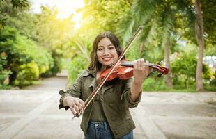 Jeune femme en jouant le violon en plein air. portrait de une fille en jouant le violon en plein air, proche en haut de une fille avec sa violon en jouant une mélodie en plein air, concept de souriant femelle violoniste photo