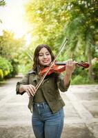 portrait de une fille en jouant le violon en plein air, proche en haut de une fille avec sa violon en jouant une mélodie en plein air, Jeune femme en jouant le violon en plein air. concept de souriant femelle violoniste photo