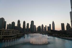 Dubai en chantant fontaines à nuit Lac vue entre grattes ciels. ville horizon dans crépuscule moderne architecture dans Émirats arabes unis Capitale centre ville. photo