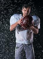 américain Football champ solitaire athlète guerrier permanent sur une champ détient le sien casque et prêt à jouer. joueur en train de préparer à courir, attaque et But atterrissage. pluvieux nuit avec spectaculaire brouillard, bleu lumière photo