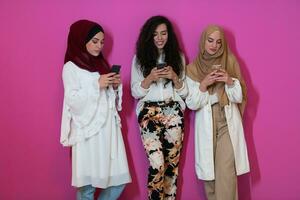 groupe de magnifique musulman femmes deux de leur dans à la mode robe avec hijab en utilisant mobile téléphone isolé sur rose Contexte représentant moderne Islam mode La technologie et Ramadan kareem concept photo