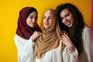 groupe portrait de magnifique musulman femmes deux de leur dans une à la mode robe avec hijab isolé sur une Jaune Contexte photo