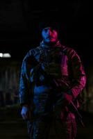 armée soldat dans combat uniformes avec un agression fusil et combat casque nuit mission foncé Contexte. bleu et violet gel lumière effet. photo