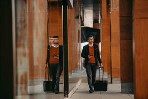 aller au terminal de l'aéroport. voyageur d'affaires confiant marchant dans les rues de la ville et tirant sa valise en buvant du café et en parlant sur un smartphone photo