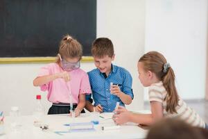 élémentaire école science salle de cours enthousiaste prof explique chimie à diverse groupe de enfants, peu garçon mélanges produits chimiques dans gobelets. les enfants apprendre avec l'intérêt photo