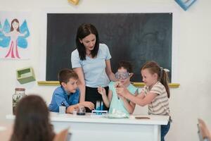 élémentaire école science salle de cours enthousiaste prof explique chimie à diverse groupe de enfants, peu garçon mélanges produits chimiques dans gobelets. les enfants apprendre avec l'intérêt photo