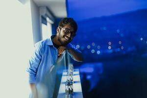 un Indien homme avec des lunettes et une bleu chemise regards autour le ville à nuit. dans le Contexte de le nuit rue de le ville photo