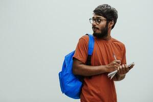 Indien étudiant avec bleu sac à dos, des lunettes et carnet posant sur gris Contexte. le concept de éducation et scolarité. temps à aller retour à école photo