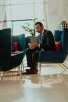 une moderne homme d'affaire dans une costume est assis dans une moderne Bureau et en utilisant sartphone. sélectif concentrer photo