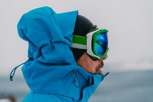 photo du visage photo de une homme dans une du froid neigeux zone portant une épais bleu hiver veste, neige des lunettes de protection et gants. la vie dans du froid Régions de le pays.