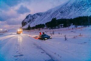 le bord de la route assistance un service tirant le voiture en dehors de le canal. un incident sur une congelé scandinave route. photo