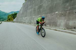 plein longueur portrait de un actif triathlète dans tenue de sport et avec une protecteur casque équitation une vélo. sélectif concentrer photo