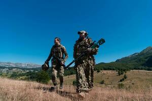 une tireur d'élite équipe équipe de soldats est Aller à l'abri. tireur d'élite assistant et équipe chef en marchant et visée dans la nature avec Jaune herbe et bleu ciel. tactique camouflage uniforme. photo