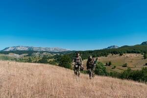 une tireur d'élite équipe équipe de soldats est Aller à l'abri. tireur d'élite assistant et équipe chef en marchant et visée dans la nature avec Jaune herbe et bleu ciel. tactique camouflage uniforme. photo