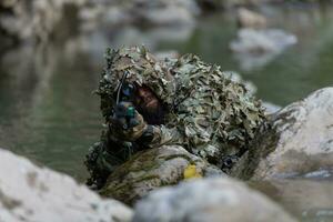 une militaire homme ou airsoft joueur dans une camouflage costume se faufiler le rivière et objectifs de une tireur d'élite fusil à le côté ou à cible. photo