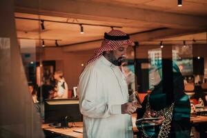 portrait photo de arabe chef homme d'affaire avec musulman hijab femme discuter affaires projets tandis que en utilisant comprimés et téléphone intelligent dans moderne verre Bureau
