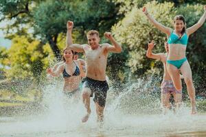 une groupe de diverse Jeune gens ayant amusement ensemble comme elles ou ils courir le long de le rivière et jouer l'eau Jeux photo