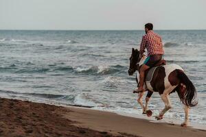 un homme moderne en vêtements d'été aime monter à cheval sur une belle plage de sable au coucher du soleil. mise au point sélective photo