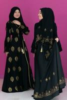 deux magnifique musulman femme dans à la mode robe avec hijab isolé sur moderne rose Contexte représentant concept de moderne Islam et Ramadan kareem photo