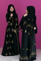 deux magnifique musulman femme dans à la mode robe avec hijab isolé sur moderne rose Contexte représentant concept de moderne Islam et Ramadan kareem photo