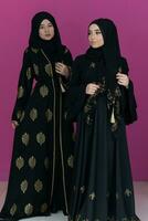 deux magnifique musulman femme dans à la mode robe avec hijab isolé sur moderne rose Contexte représentant concept de moderne Islam et Ramadan kareem photo