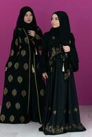 deux magnifique musulman femme dans à la mode robe avec hijab isolé sur moderne rose Contexte représentant concept de moderne Islam et Ramadan kareem photo