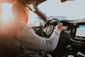 une homme avec une des lunettes de soleil conduite une voiture à le coucher du soleil. le concept de voiture Voyage photo