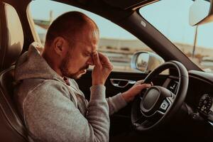 une fatigué chauffeur en portant le sien diriger. épuisé et fatigué chauffeur conduite une voiture à le coucher du soleil photo