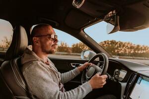 une homme avec une des lunettes de soleil conduite une voiture à le coucher du soleil. le concept de voiture Voyage photo