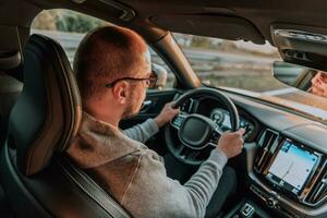 une homme avec une des lunettes de soleil conduite une voiture à le coucher du soleil. le concept de voiture Voyage photo