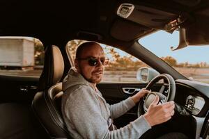 une homme avec une des lunettes de soleil conduite une voiture à le coucher du soleil. le concept de voiture Voyage photo