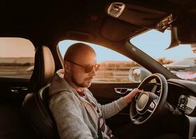 une homme avec une des lunettes de soleil conduite une voiture à le coucher du soleil. le concept de voiture Voyage photo