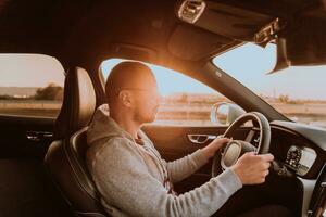 une homme avec une des lunettes de soleil conduite une voiture à le coucher du soleil. le concept de voiture Voyage photo