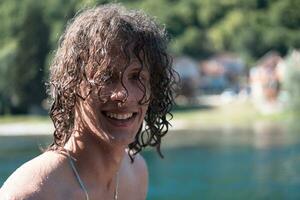 portrait de une Jeune adolescent garçon avec frisé humide cheveux près le rivière ayant amusement avec copains à une été faire la fête. photo