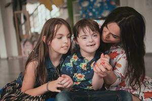 une fille et une femme étreinte une enfant avec vers le bas syndrome dans une moderne préscolaire institution photo