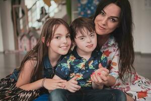 une fille et une femme étreinte une enfant avec vers le bas syndrome dans une moderne préscolaire institution photo