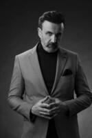 portrait d'un homme d'affaires senior élégant et élégant avec une barbe et des vêtements d'affaires décontractés en studio photo isolé sur fond sombre gesticulant avec les mains
