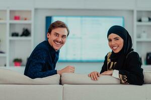 Jeune musulman couple femme portant islamique hijab vêtements séance sur canapé en train de regarder la télé ensemble pendant le mois de Ramadan à moderne Accueil photo