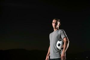 portrait de une Jeune Beau football joueur homme sur une rue en jouant avec une Football balle. photo