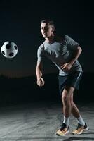 portrait de une Jeune Beau football joueur homme sur une rue en jouant avec une Football balle. photo