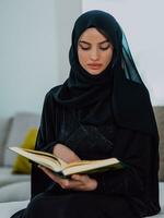 Jeune traditionnel musulman femme en train de lire coran sur le canapé avant iftar dîner pendant une Ramadan le banquet à Accueil photo