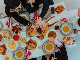 Haut vue de musulman famille ayant iftar dîner en buvant l'eau à Pause festin. en mangeant traditionnel nourriture pendant Ramadan festoyer mois à maison. le islamique halal en mangeant et en buvant dans moderne Accueil photo