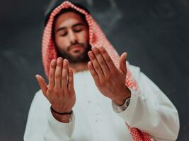 arabe homme dans traditionnel vêtements fabrication traditionnel prière à Dieu, garde mains dans prier geste dans de face de noir tableau noir représentant moderne Islam mode et Ramadan kareem concept photo