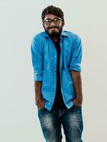 Indien souriant Jeune homme avec bleu chemise et des lunettes posant sur gris Contexte photo