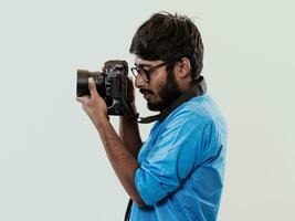 professionnel photographe ayant dslr caméra prise photo.indien homme la photographie passionné prise photo tandis que permanent sur bleu Contexte. studio coup